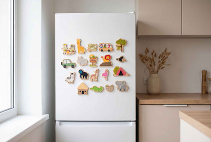 Eine Sammlung von Holzmagneten mit Tieren, darunter eine Giraffe, ein Zebra und ein Elefant, wird auf einem weißen Kühlschrank präsentiert. Weitere Magnete zeigen ein Auto, ein Haus und ein Zelt. Die Magnete sind in verschiedenen Farben und Formen.